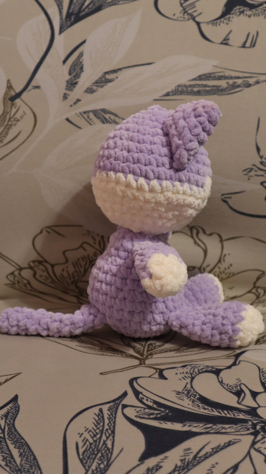 Side view of a crocheted purple and white kitten plushie on a floral fabric background