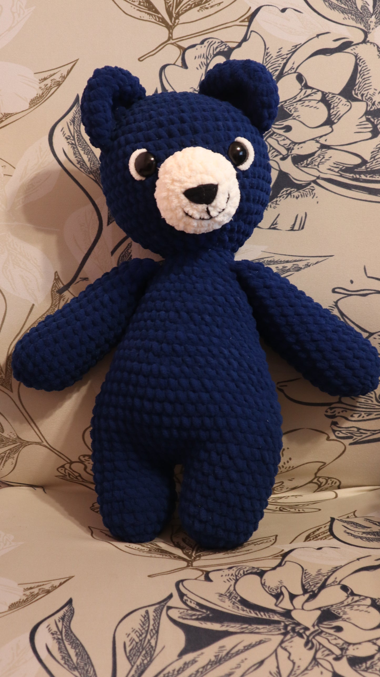 Dark Blue crocheted bear on a floral-patterned fabric background