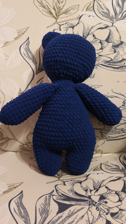 Back view of a dark Blue crocheted bear on a floral-patterned fabric background