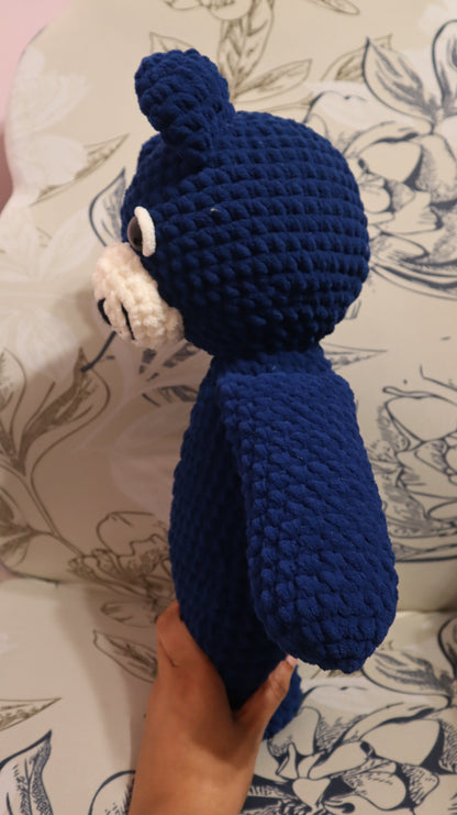 Side view of a dark Blue crocheted bear on a floral-patterned fabric background