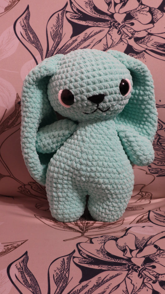 Crocheted seafoam green bunny plushie  on a floral fabric background