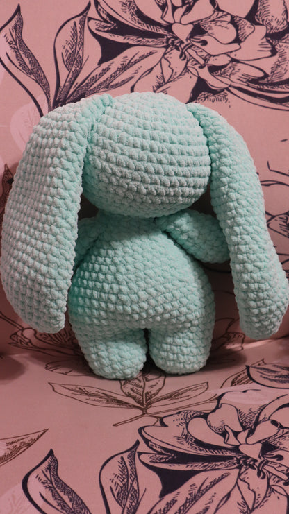 Back view of a crocheted seafoam green bunny plushie  on a floral fabric background