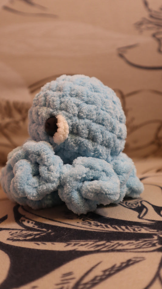 Side view of a light blue crocheted Octopus plushie on a floral fabric background