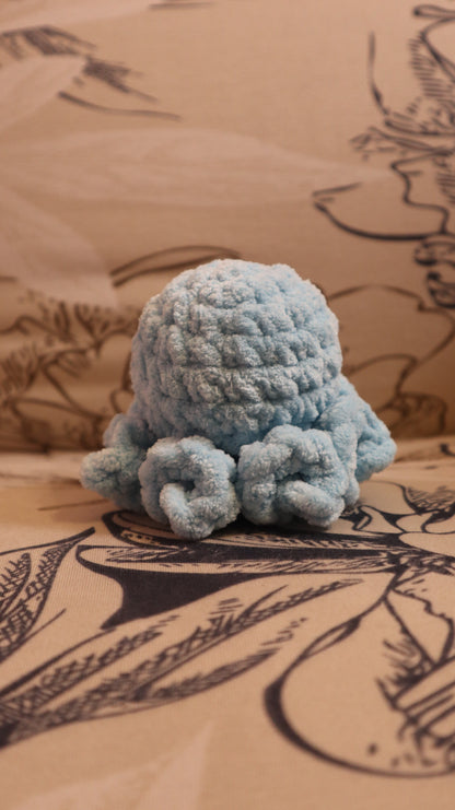 Back view of a light blue crocheted Octopus plushie on a floral fabric background