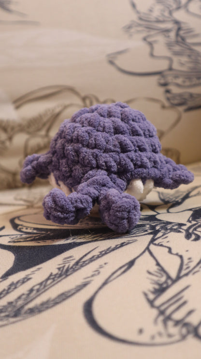Back view of a dark purple and white crocheted whale plushie on a floral pattern fabric background